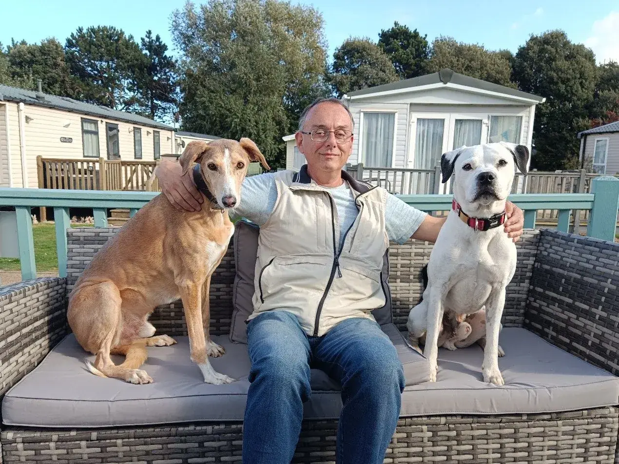 Guest sitting on the Tern 32 deck sofa with two dogs beside him, with turquoise railings and caravans behind