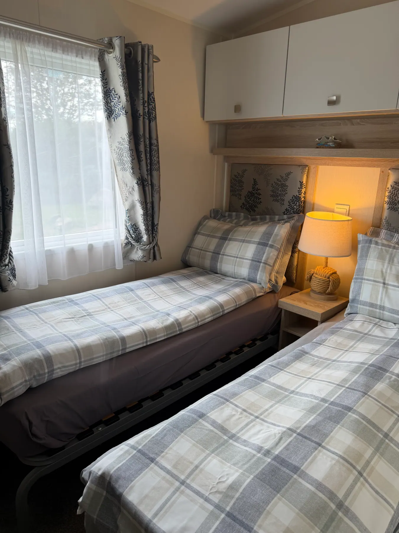 Twin bedroom inside Tern 32 with two single beds in blue-and-white plaid bedding, overhead cupboards and patterned curtains