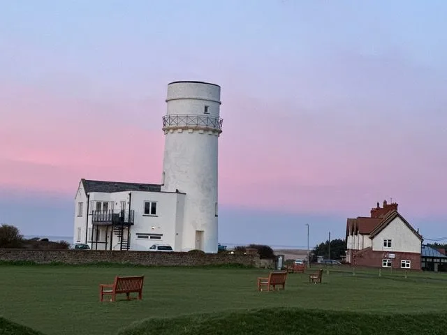 A white round old tower beside a green with benches under a pink and lilac sky