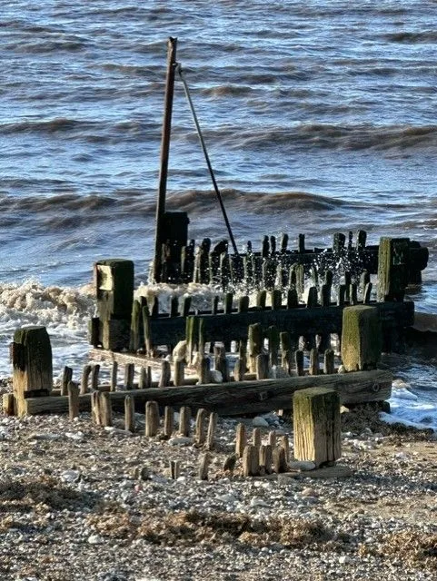 Weathered wooden groynes with waves breaking over them on a shingle beach