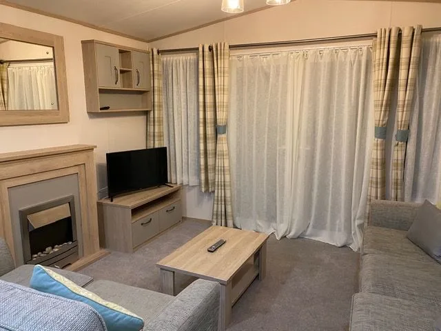 The lounge inside Windsor 30 with grey sofas, an electric fire in a wooden surround and a television