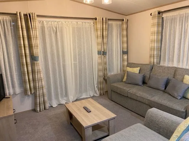The lounge inside Windsor 30 with a grey sofa, patterned cushions, a wooden coffee table and checked curtains with tie-backs