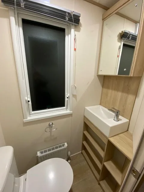 The separate toilet and washroom inside Windsor 30 with a white toilet, a basin, a mirror, a frosted window and a heated towel rail