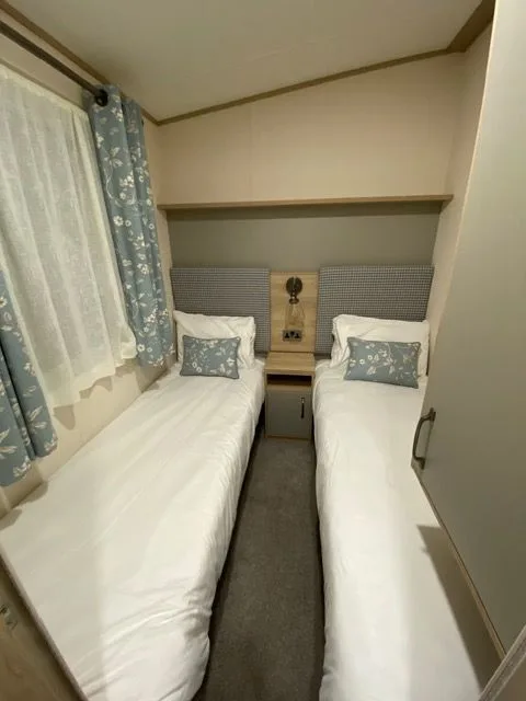 A twin bedroom inside Windsor 30 with two single beds, white bedding, blue floral cushions and blue floral curtains